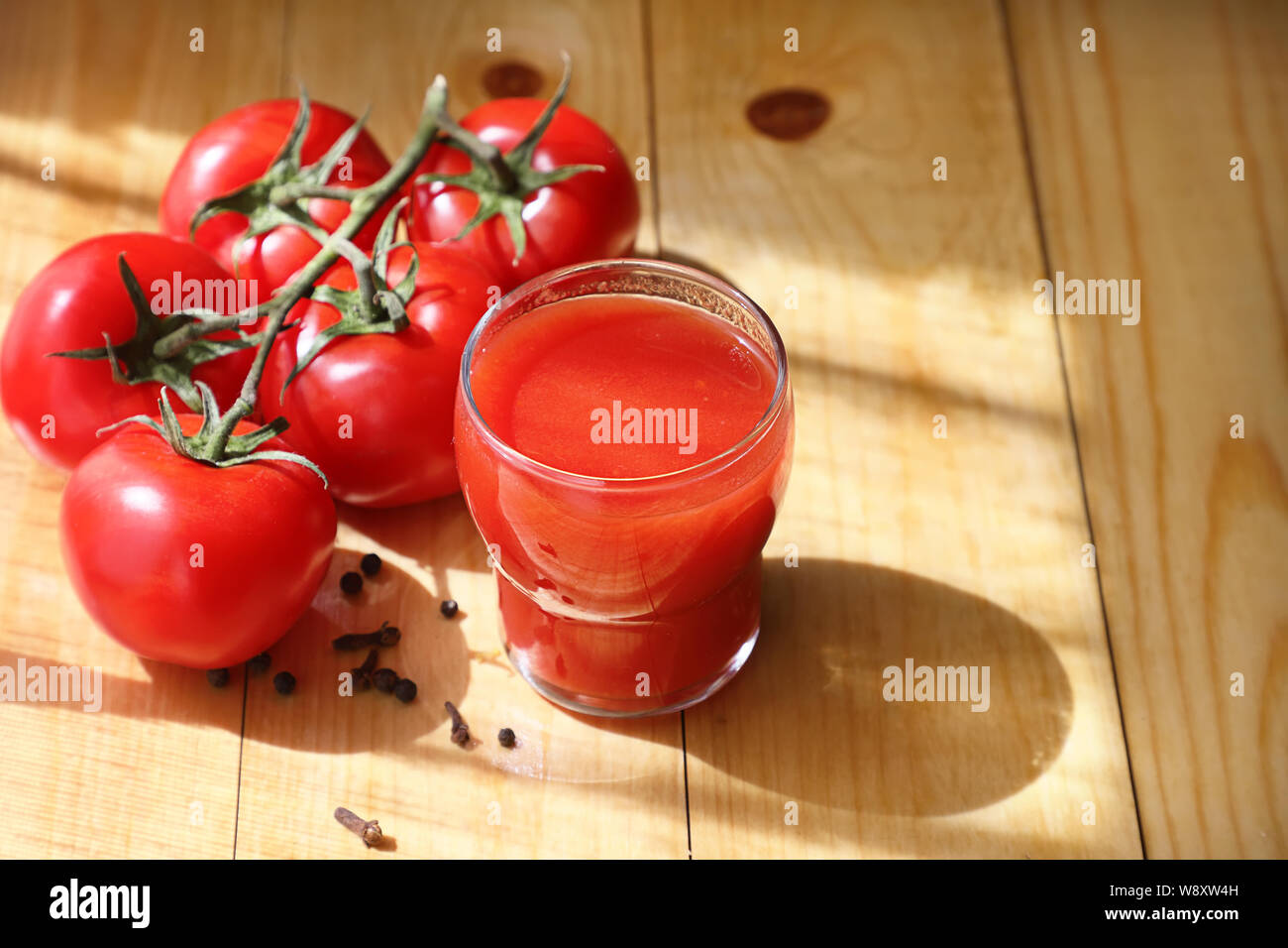 Du jus de tomate dans une tasse en verre avec un tas de tomates mûres, sur un fond en bois clair.copier l'espace. Banque D'Images