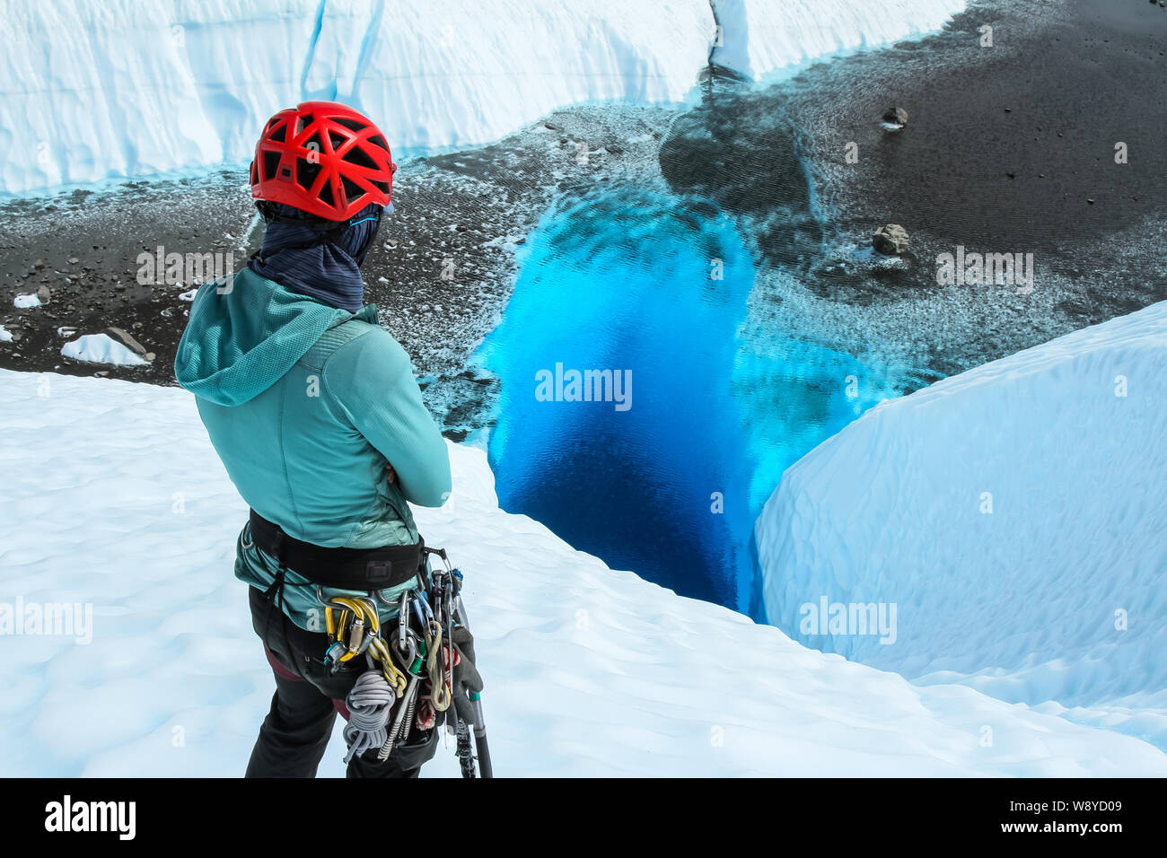 Une jeune femme se tient avec les bras croisés le fixer un trou bleu profond rempli d'eau sur la Matanuska Glacier en Alaska. Banque D'Images