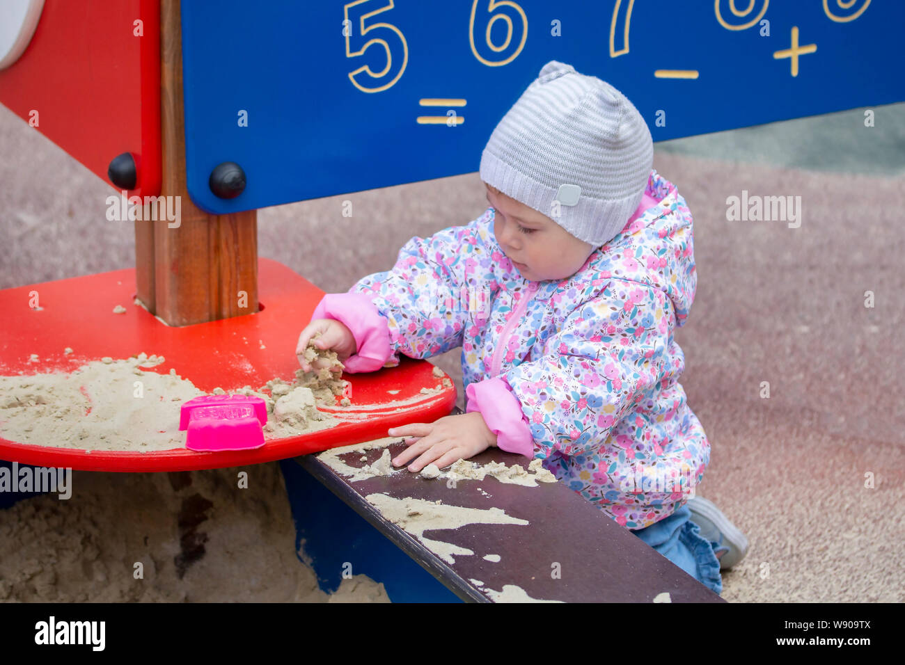 Bébé fille jouant avec le sable. Une fille dans une rose et un chapeau pour une promenade joue avec du sable dans un bac à sable, ramasse le sable, le monde autour d'études. Un petit Banque D'Images