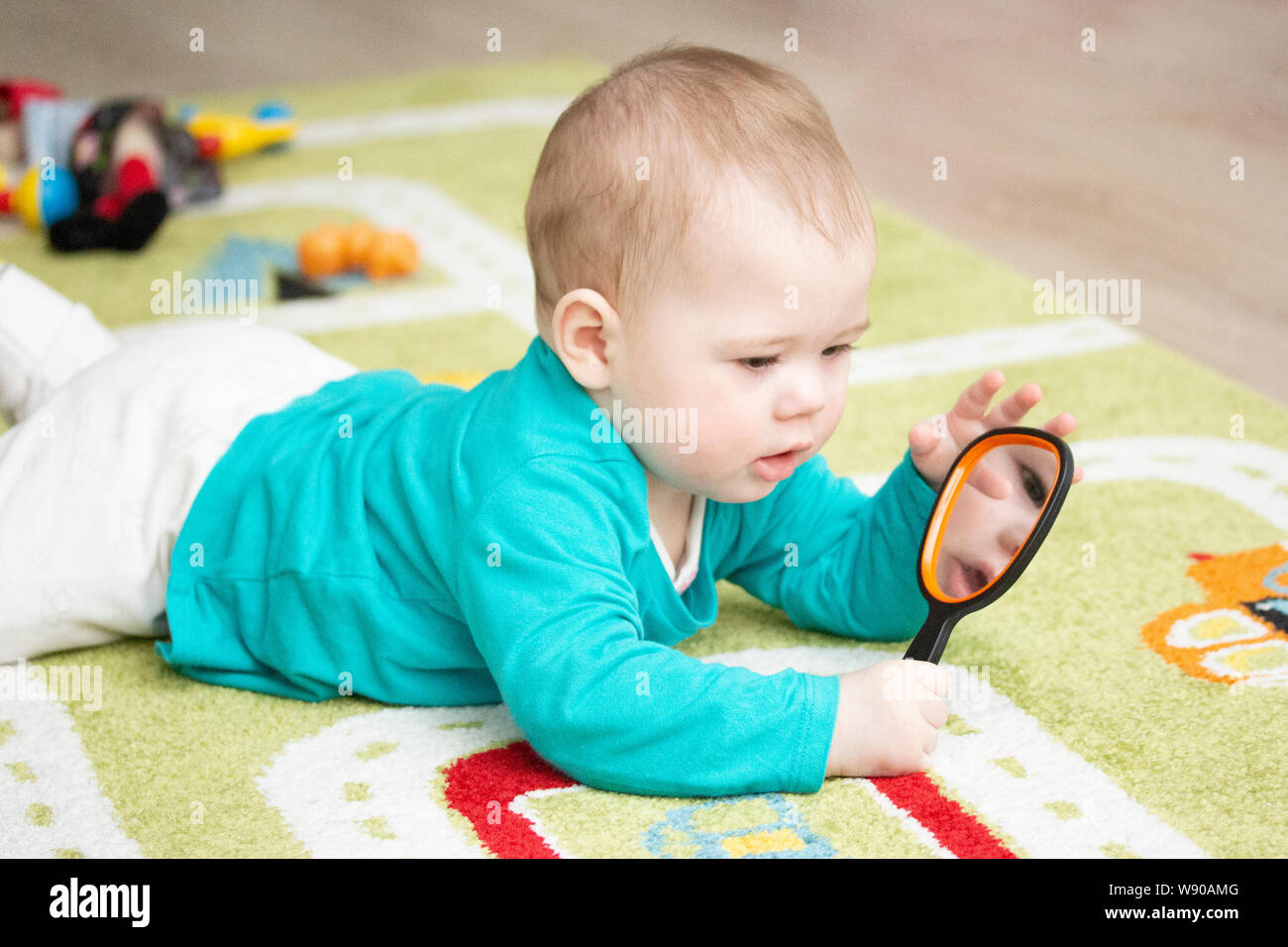 Un enfant de 7 mois examine lui-même dans un miroir posé sur un tapis de  couleur claire. Bébé Garçon Fille jouant avec un miroir gisant sur le sol.  Portrait Kid Soft Focu