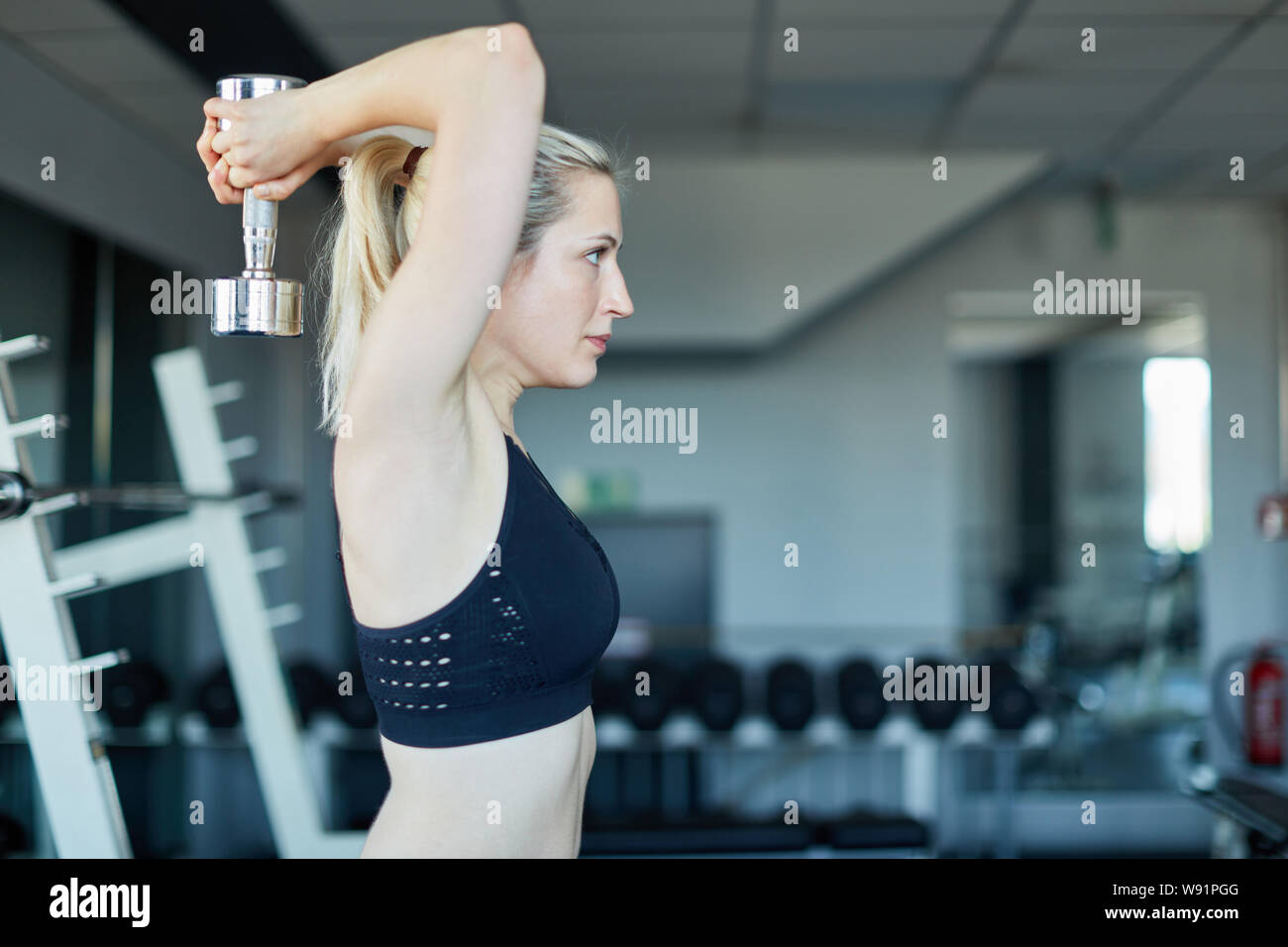 Jeune femme faisant un exercice triceps avec un haltère dans la salle de sport Banque D'Images