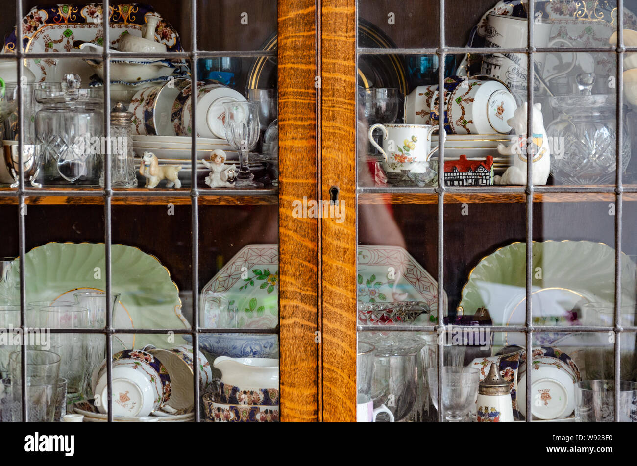 Vue rapprochée d'assiettes, de tasses, soucoupes et d'objets de collection sur une étagère dans un cabinet d'affichage en verre. Banque D'Images