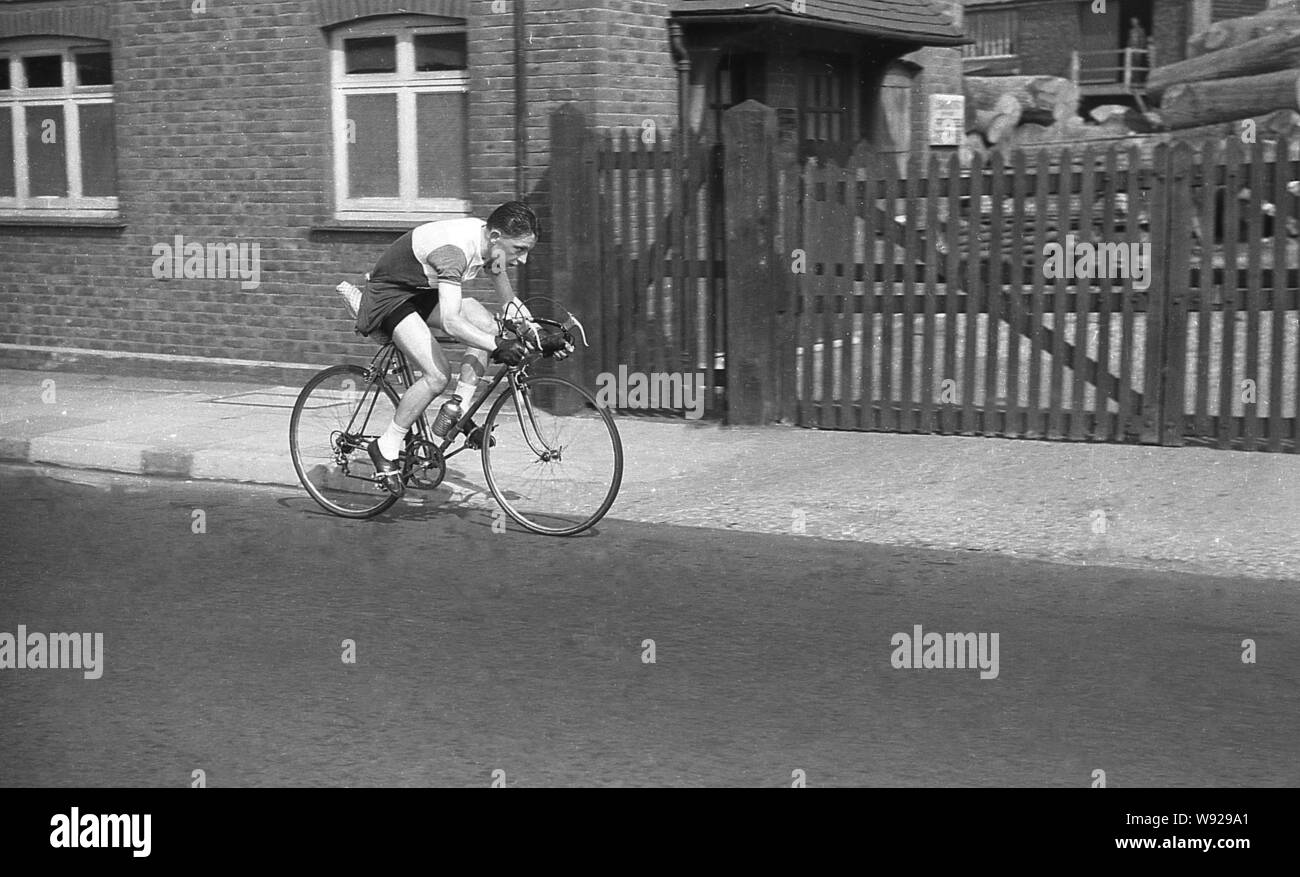 Années 1950, historique, un coureur cycliste masculin sur le cyclisme sur route au-delà d'un parc à bois, l'île de Man. Banque D'Images