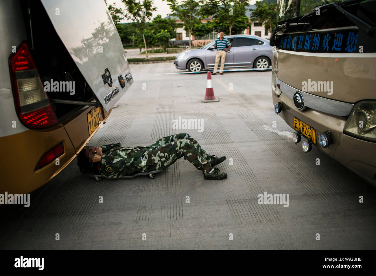 Un soldat de la défense de la frontière chinoise se glisse sous un bus pour recherche de médicaments à un point de contrôle près de la frontière de la Chine et du Myanmar à Mengyang ville, Jinghon Banque D'Images