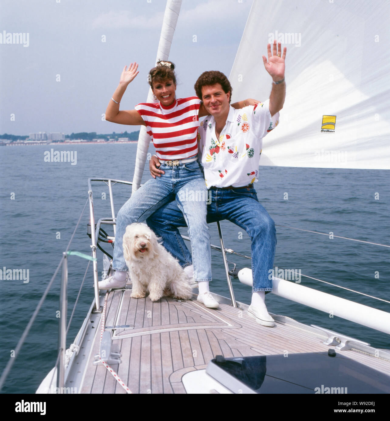 Die britische-Schlagersängerin deusch Sheer Ireen posiert langhaarigen Tibet-Terrier mit ihrem und ihrem Ehemann Gavin du Porter auf einem Segelboot, fin des années 80 er Jahren. La chanteuse pop anglo-allemande pure Ireen pose fièrement avec son poil long terrier du Tibet et son mari Gavin du Porter sur un bateau à voile à la fin des années 1980. Banque D'Images