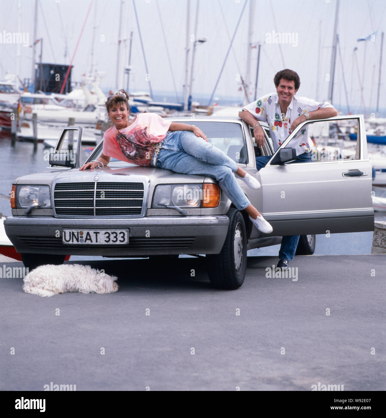 Die britische-Schlagersängerin deusch Sheer Ireen posiert langhaarigen Tibet-Terrier mit ihrem und ihrem Ehemann Gavin du Porter auf einer Mercedes S-Klasse vor einem Hafen, fin des années 80 er Jahren. La chanteuse pop anglo-allemande pure Ireen pose fièrement avec son poil long terrier du Tibet et son mari Gavin du porter sur une Mercedes classe S en face d'un port à la fin des années 80. Banque D'Images