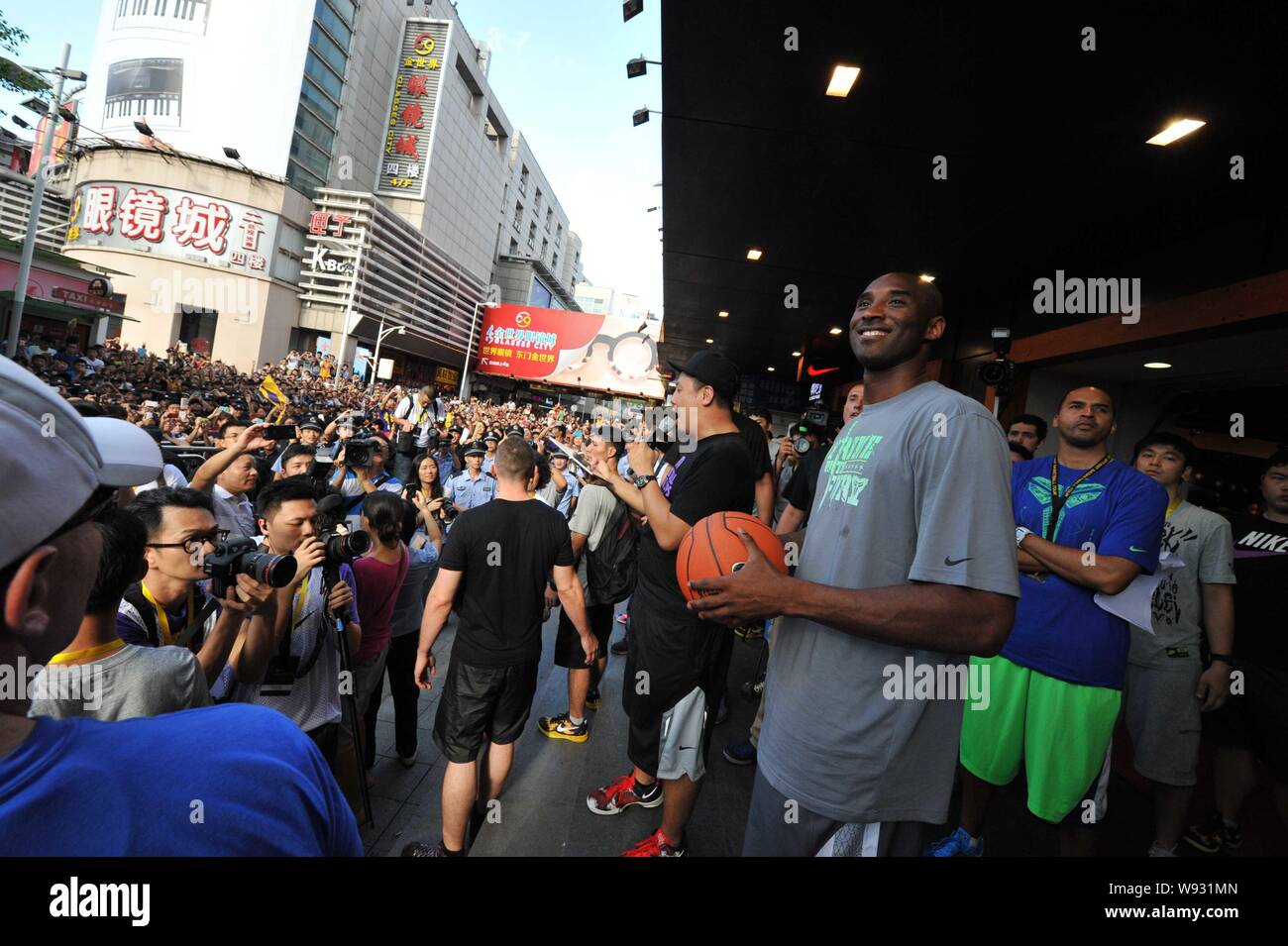 Star de la NBA Kobe Bryant, avant, sourit avant de lancer un ballon de basket à une foule de fans lors d'un événement promotionnel dans un magasin de vêtements de sport Nike dans un magasin Banque D'Images
