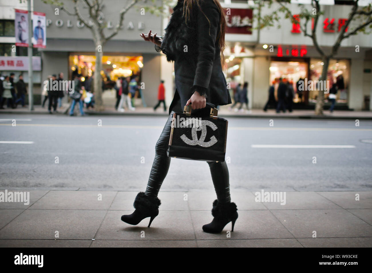 --FILE--une femme portant un sac à main Chanel utilise son téléphone mobile comme elle marche sur une route à Shanghai, Chine, 11 décembre 2013. Les Chinois seuls cordons ombilicaux vers l Banque D'Images