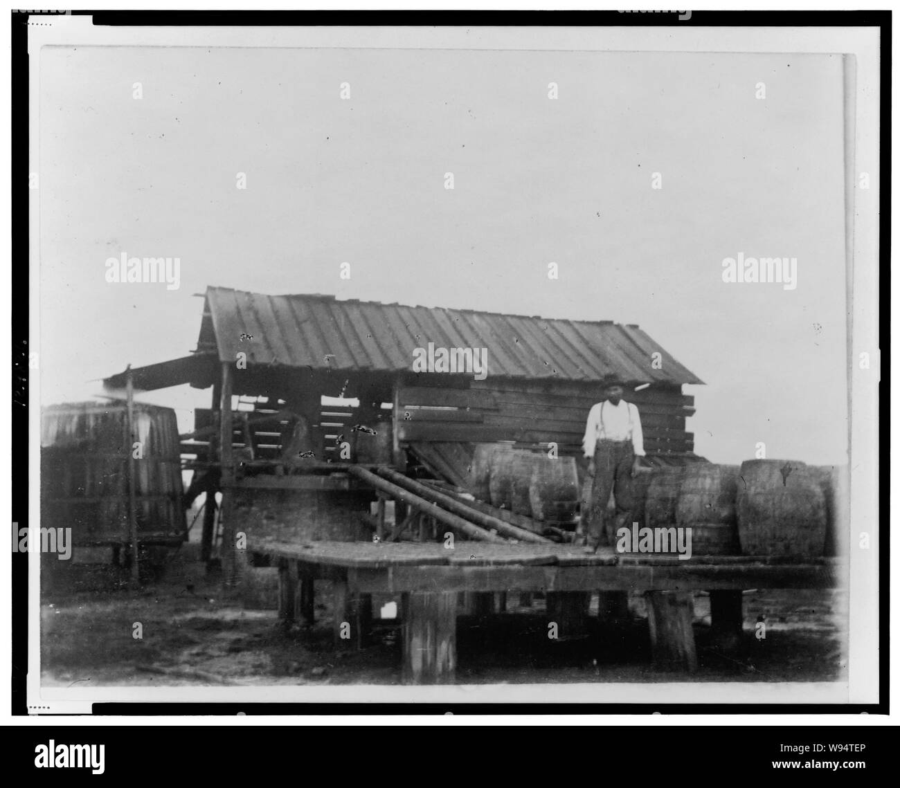 African American man standing on platform ou quai de chargement avec de grands fûts et une rampe pour une structure dans l'arrière-plan avec un grand bac ou silo, en Géorgie Banque D'Images