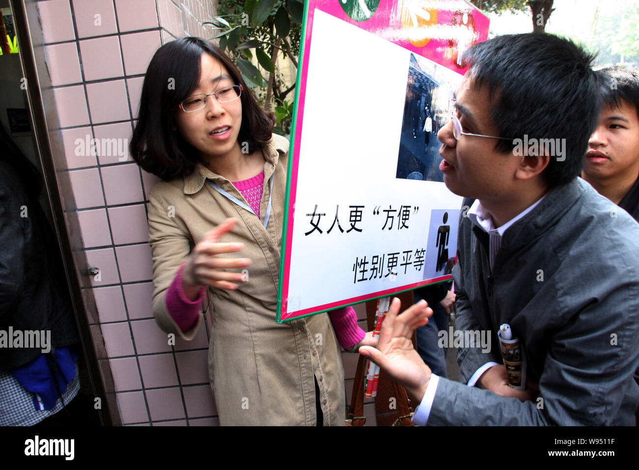 Un étudiant chinois femelle est titulaire d'une bannière et des protestations devant les toilettes publiques appelant à plus de cellules pour les femmes occupent au cours d'une mens toilettes déplacer Banque D'Images