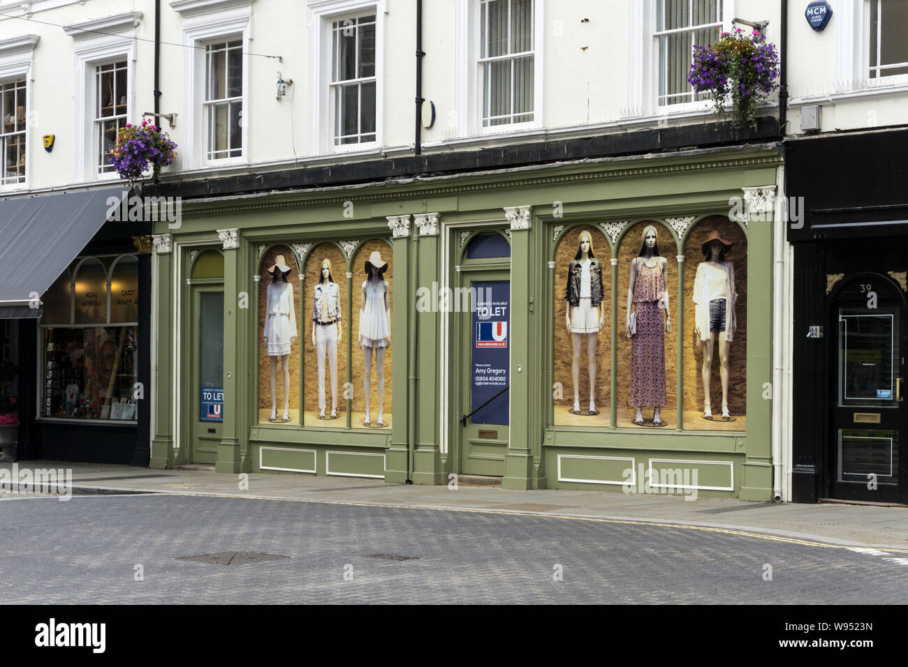 La façade double vide shop locaux précédemment occupés par Adams Boulangerie, St Giles St, Norethampton, Royaume-Uni ; fenêtres décorées par des posters de mannequins Banque D'Images