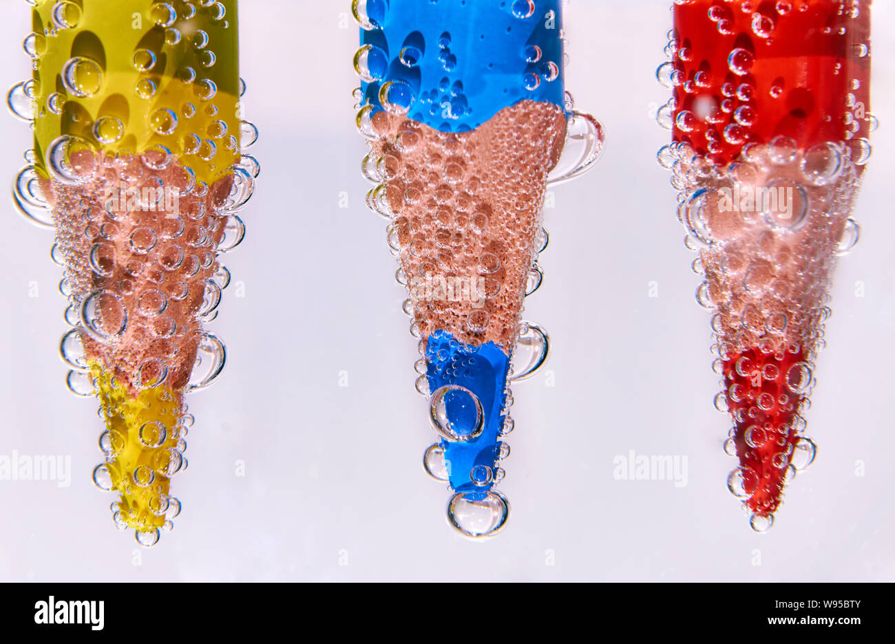 Trois crayons de couleur dans de l'eau gazeuse sur fond blanc Banque D'Images
