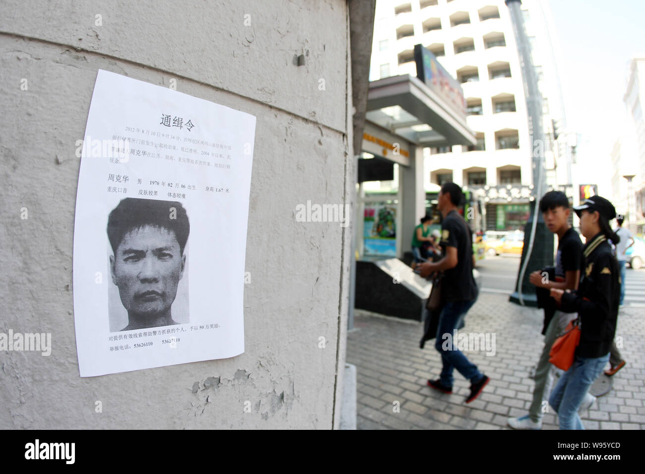 Les piétons à pied passé un avis de la police de la chasse à l'homme d'être un tueur en série Zhou Kehua à Harbin City, Heilongjiang province nord-est de Chines, 13 août 20 Banque D'Images