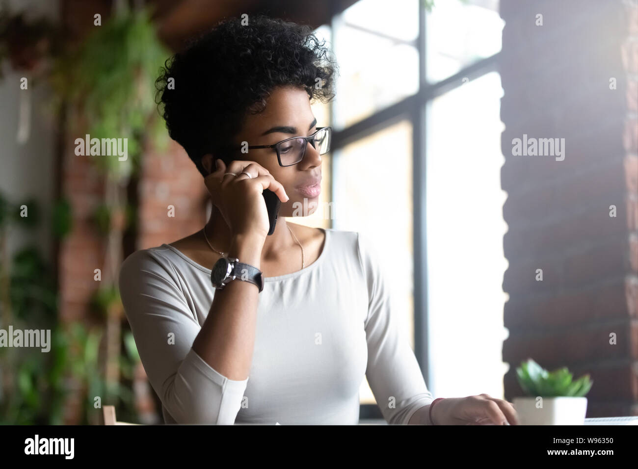 Pensive femelle biracial talking on cellphone occupé au travail Banque D'Images