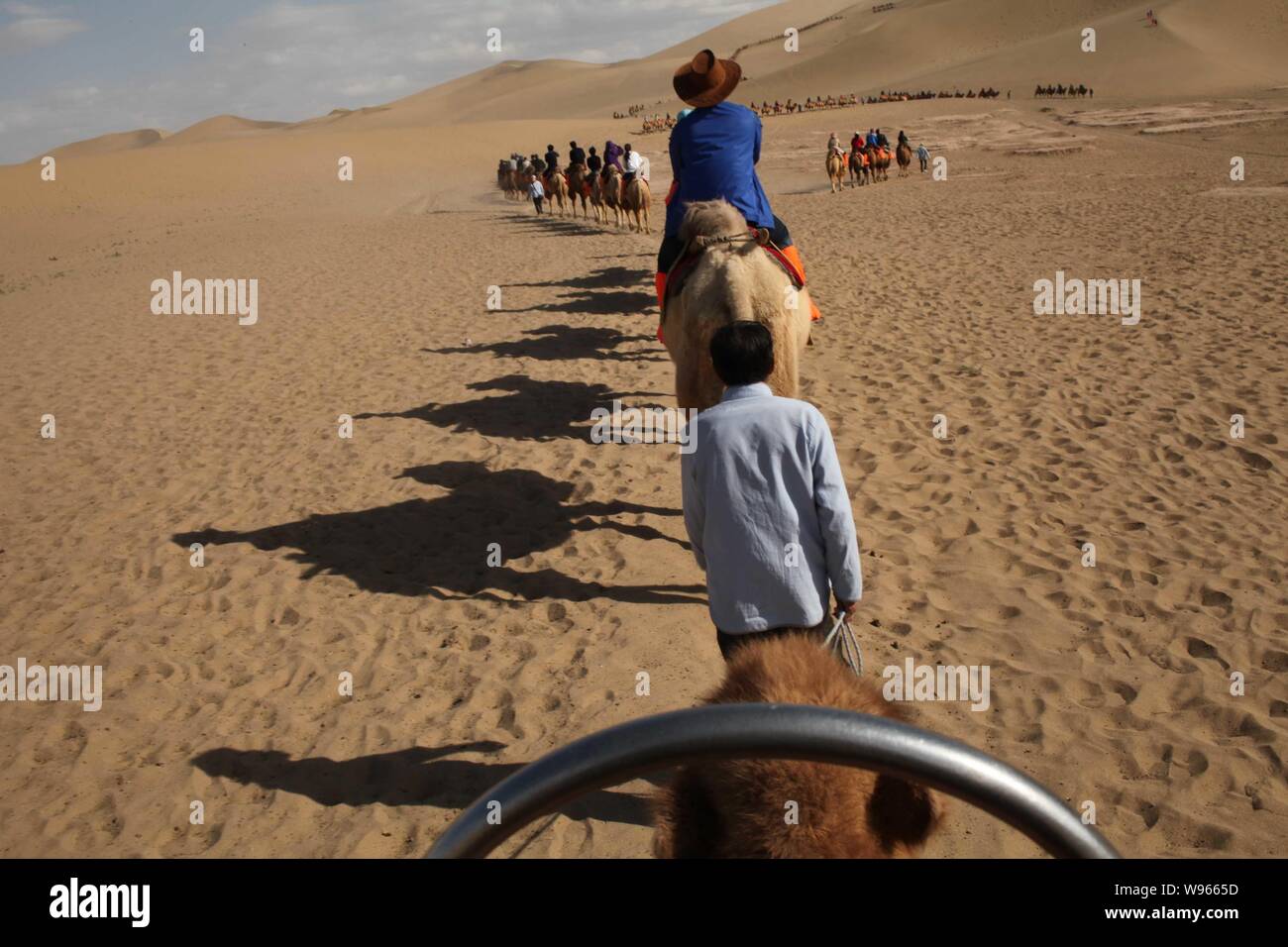 Les touristes monter des chameaux dans le désert dans le Croissant de lune (Yueyaquan) et le chant des montagnes de sable dans endroit pittoresque, au nord-ouest de la ville de Dunhuang Chines Banque D'Images