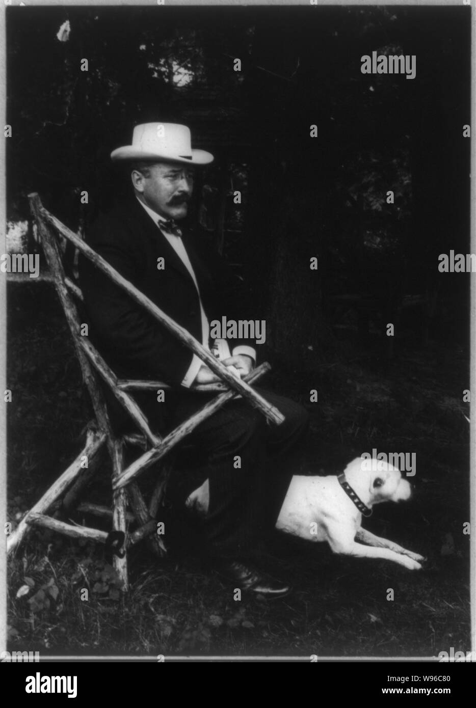 Brooks Alton Parker, 1852-1926, portrait, assis dans fauteuil rustique, faisant face à droite avec chien sur pelouse wearing straw hat Banque D'Images