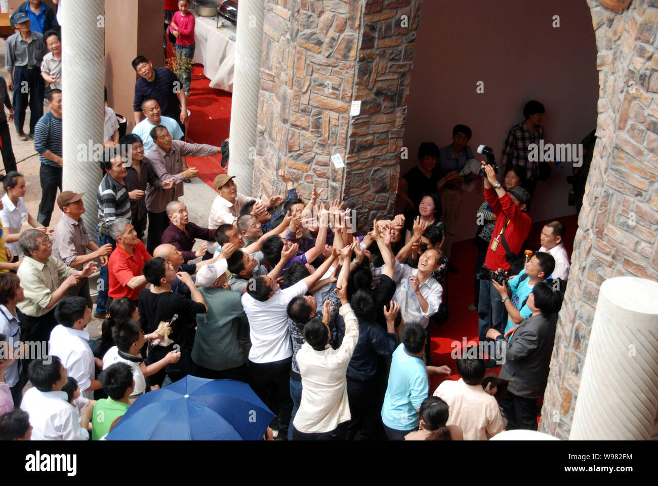 Une foule de personnes essayer de saisir les factures RMB étant dispersées par des jeunes femmes de la deuxième étage d'une villa lors d'un événement promotionnel pour une pr Banque D'Images