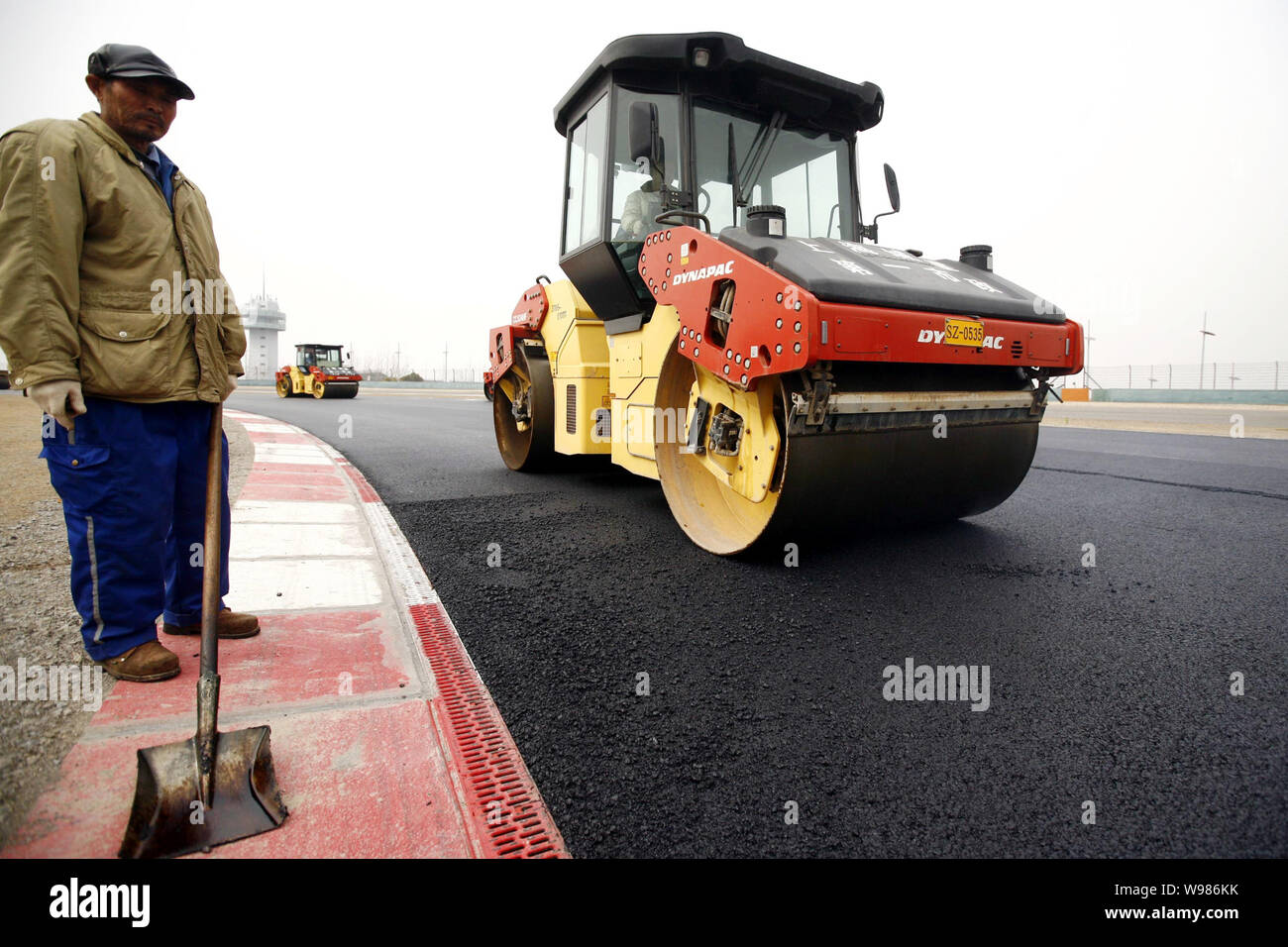 Les travailleurs chinois de la route d'entraînement des rouleaux pour le nouveau niveau de la couche d'asphalte sur la piste sur le Circuit International de Shanghai à Shanghai, Chine, 15 mars 2011 Banque D'Images