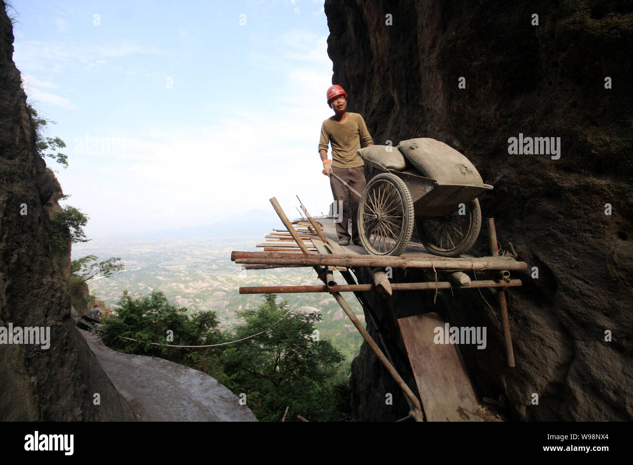 Un travailleur transporte des matériaux de construction sur un chemin en bois pour construire une route sur la falaise de Shifo en montagne l'endroit pittoresque Shiniuzhai en pays Pingjiang Banque D'Images