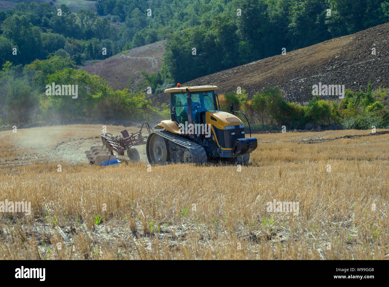 Toscane, Italie - 23 septembre 2017 : chenille jaune tracteur avec une charrue sur un champ fauché sur un jour de septembre Banque D'Images