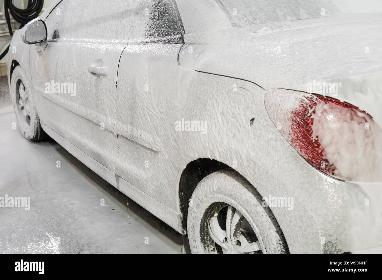 Voiture est recouverte de mousse blanche dans le lavage de voiture dans le garage. Les lave-linge. De lavage automatique. Banque D'Images