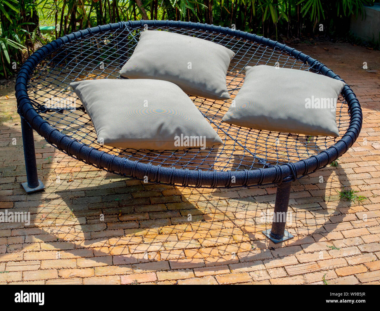 Macrame rond noir canapé-lit sur plusieurs cordes avec trois oreillers sur sol en brique dans le jardin. Banque D'Images