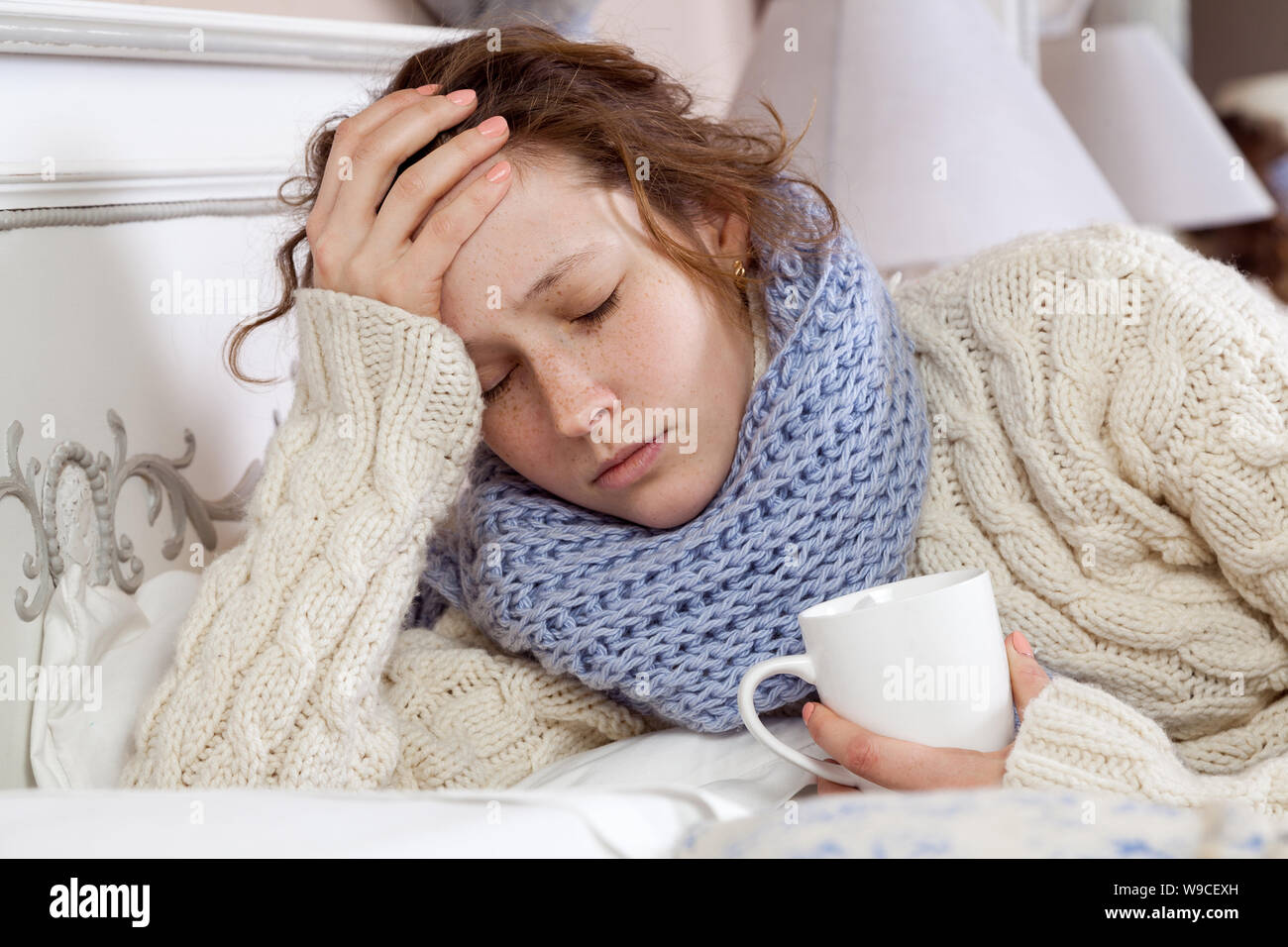 Seul triste jeune femme en pull blanc et bleu foulard de tête, sensation de froid et de repos maladie accueil au lit. tenant sa tête douloureuse et penser à ce que Banque D'Images