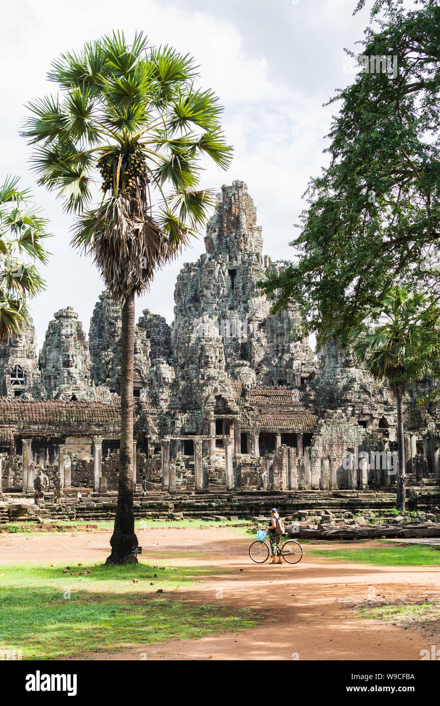 Young woman riding bicycle à côté d'anciennes ruines du temple Bayon à Angkor Wat, au Cambodge complexe. Orientation verticale Banque D'Images