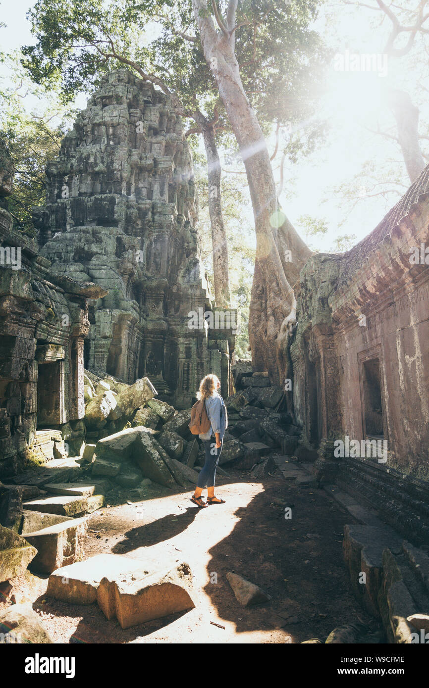 Young blonde woman découvrir les ruines du temple d'Angkor Wat à Siem Reap, Cambodge. Arbre qui pousse sur le toit de temple. Banque D'Images