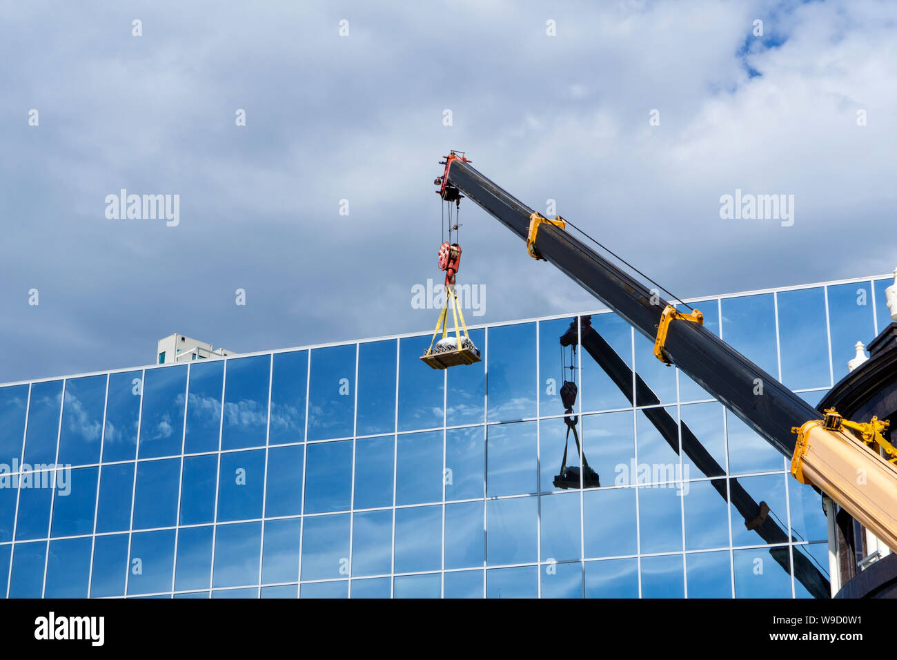 Bras télescopique d'une grue de construction des ascenseurs la charge contre le mur miroir de l'immeuble qui reflètent le ciel Banque D'Images