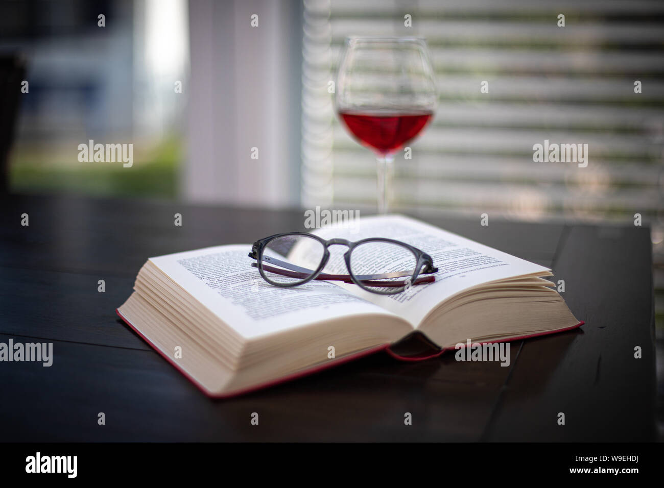 Une paire de lunettes se trouve sur un livre ouvert et à l'arrière-plan est un verre à vin Banque D'Images