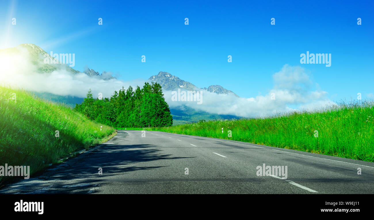 Route asphaltée entre les champs sur fond d'un paysage de montagne. Banque D'Images