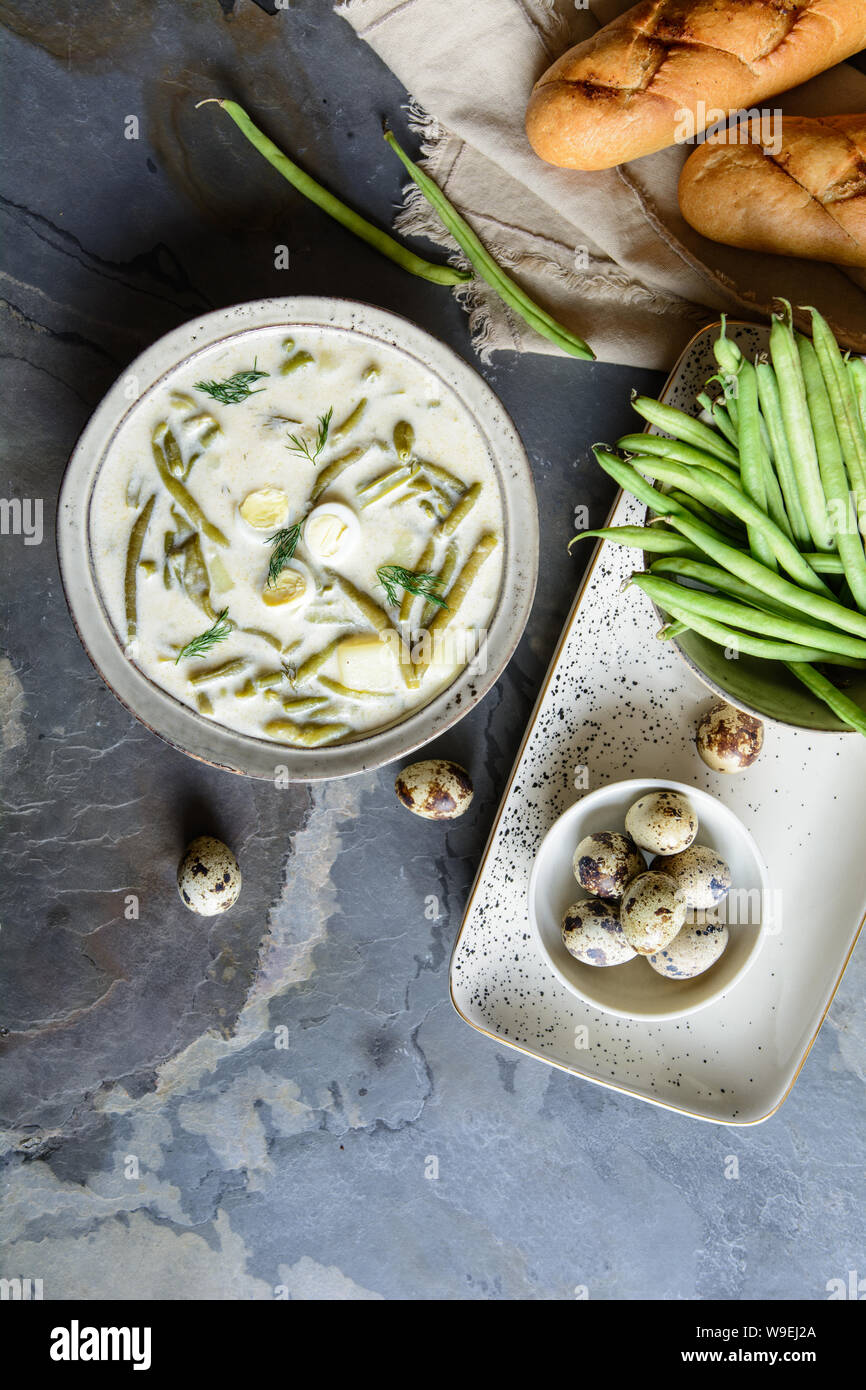 Soupe aux haricots verts produits laitiers avec des pommes de terre et de l'aneth dans un bol en céramique servi avec pain baguette Banque D'Images