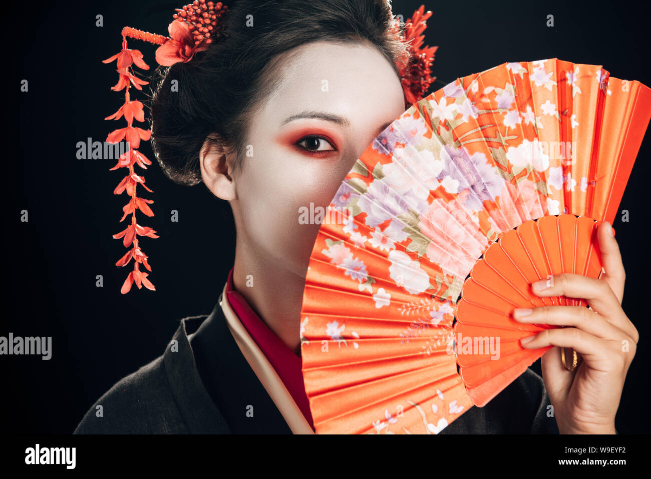 Belle geisha rouge avec des fleurs dans les cheveux maintenant ventilateur traditionnel isolated on black Banque D'Images