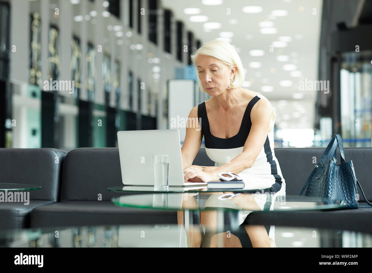 Serious mature businesswoman avec de courts cheveux blonds assis à la table et se concentrer sur son travail elle typing on laptop at office Banque D'Images