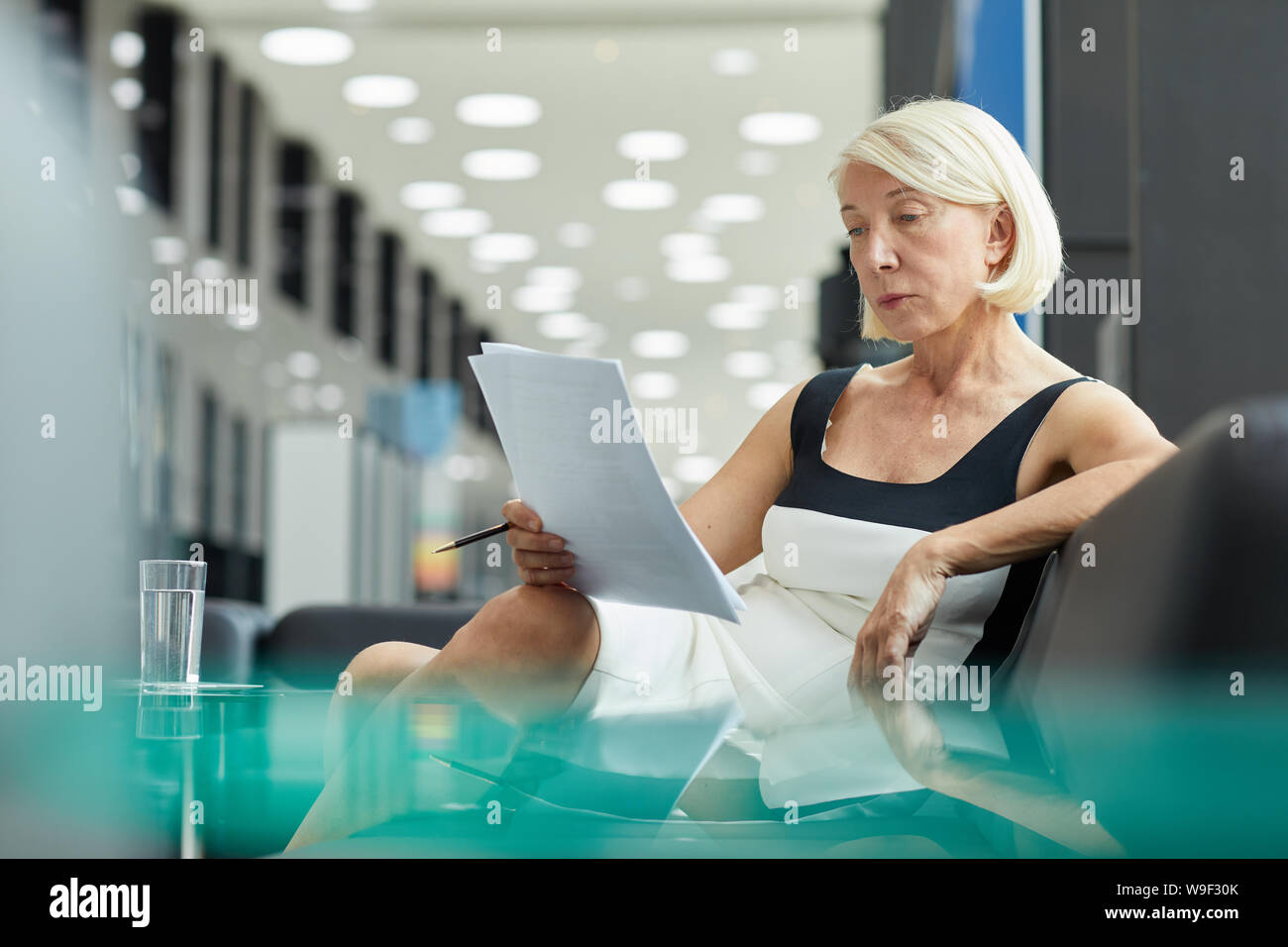 Femme sérieuse mature aux cheveux courts assise sur un canapé et la lecture de documents avant la réunion d'affaires Banque D'Images