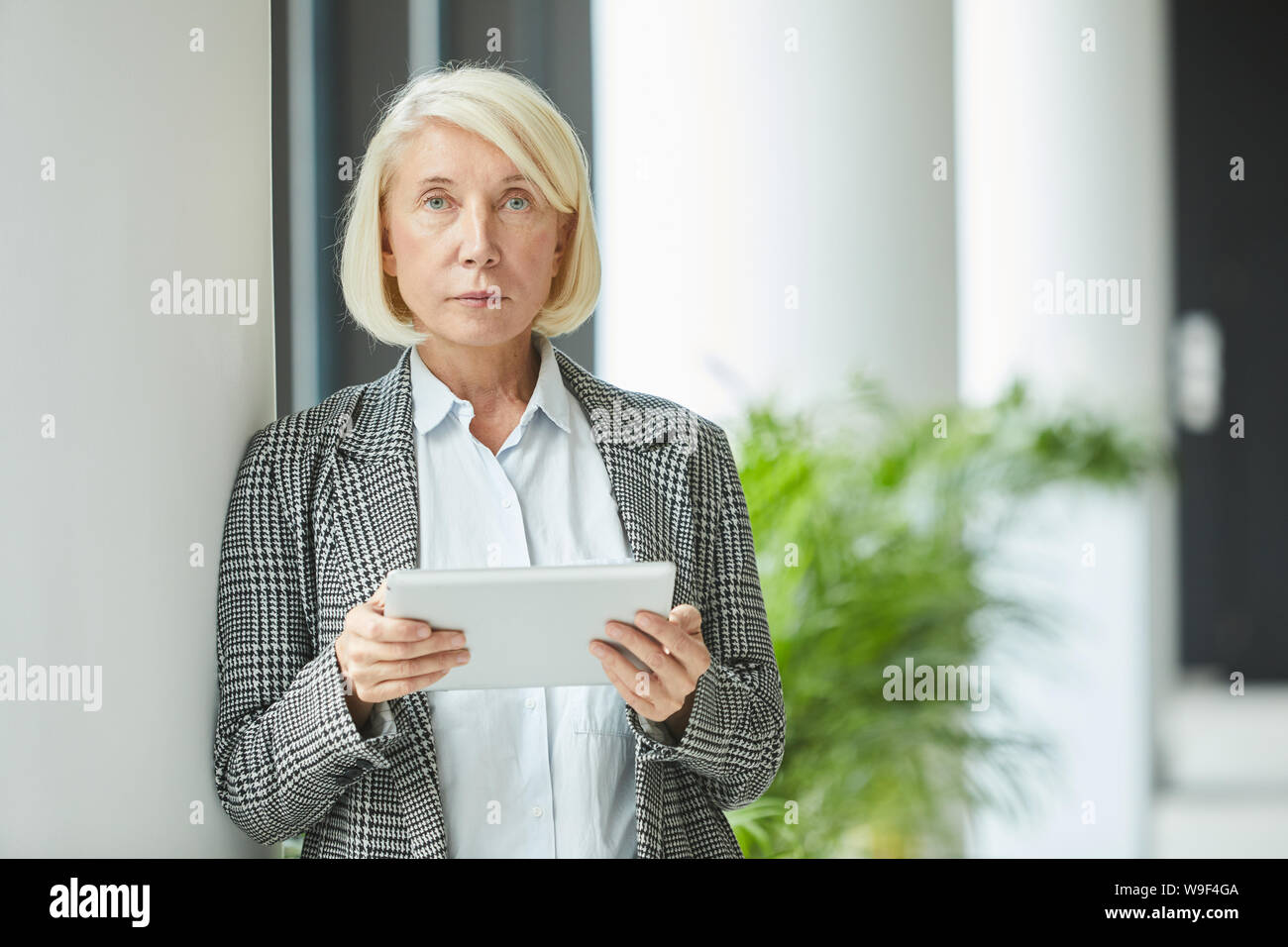 Portrait of serious mature businesswoman avec de courts cheveux blonds looking at camera while using digital tablet Banque D'Images