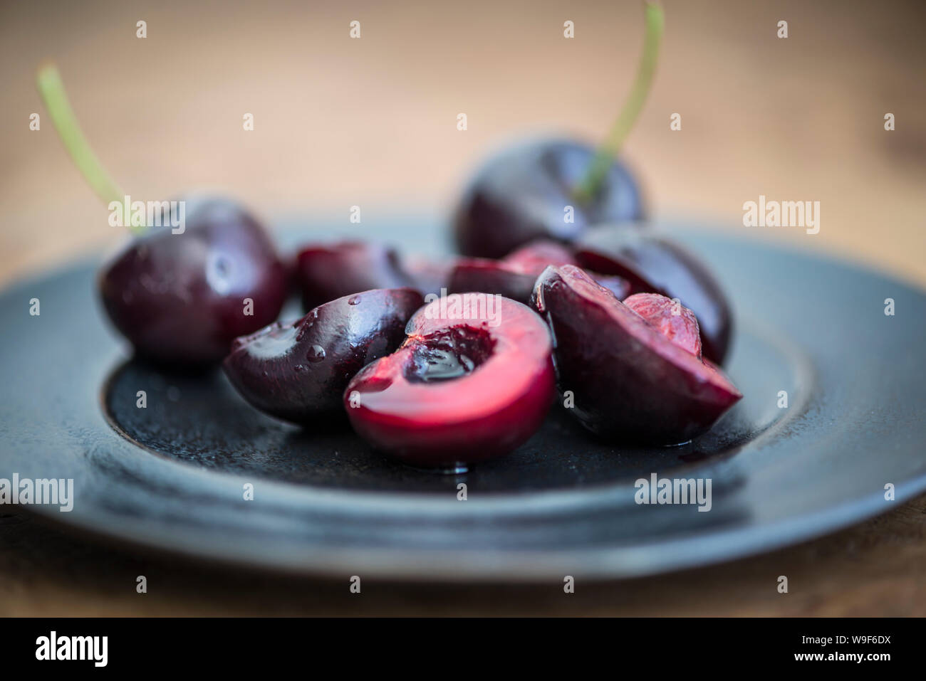 Cerises fraîches sur une plaque noire, certains coupés en deux, certains avec des tiges. Banque D'Images