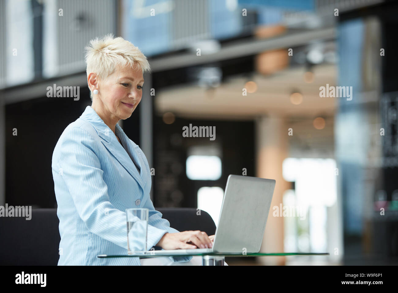 Femme mature aux cheveux courts assise à la table et de la saisie sur ordinateur portable elle travail en ligne Banque D'Images