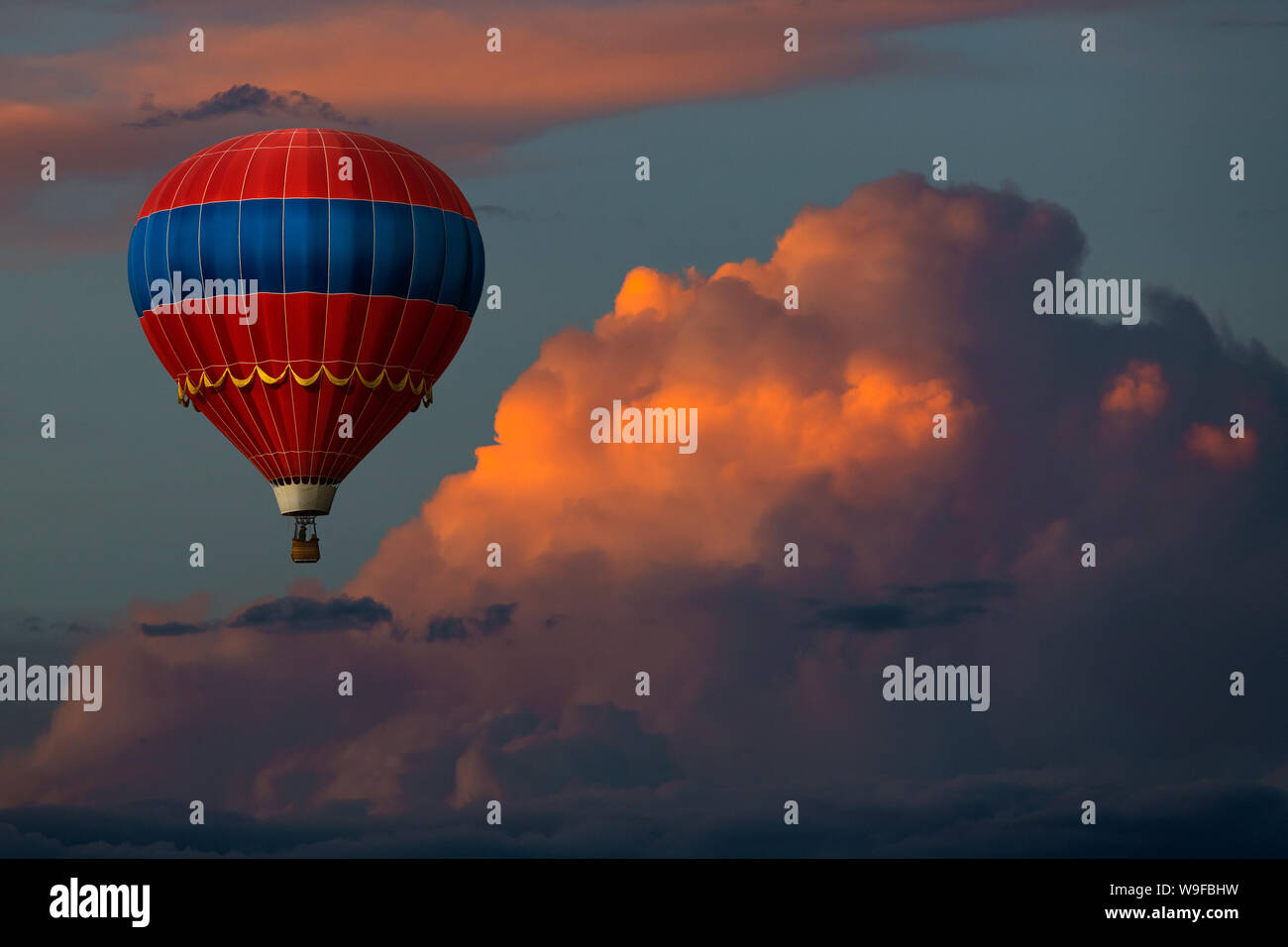 Red hot air balloon floating dans de beaux nuages colorés au coucher du soleil Banque D'Images