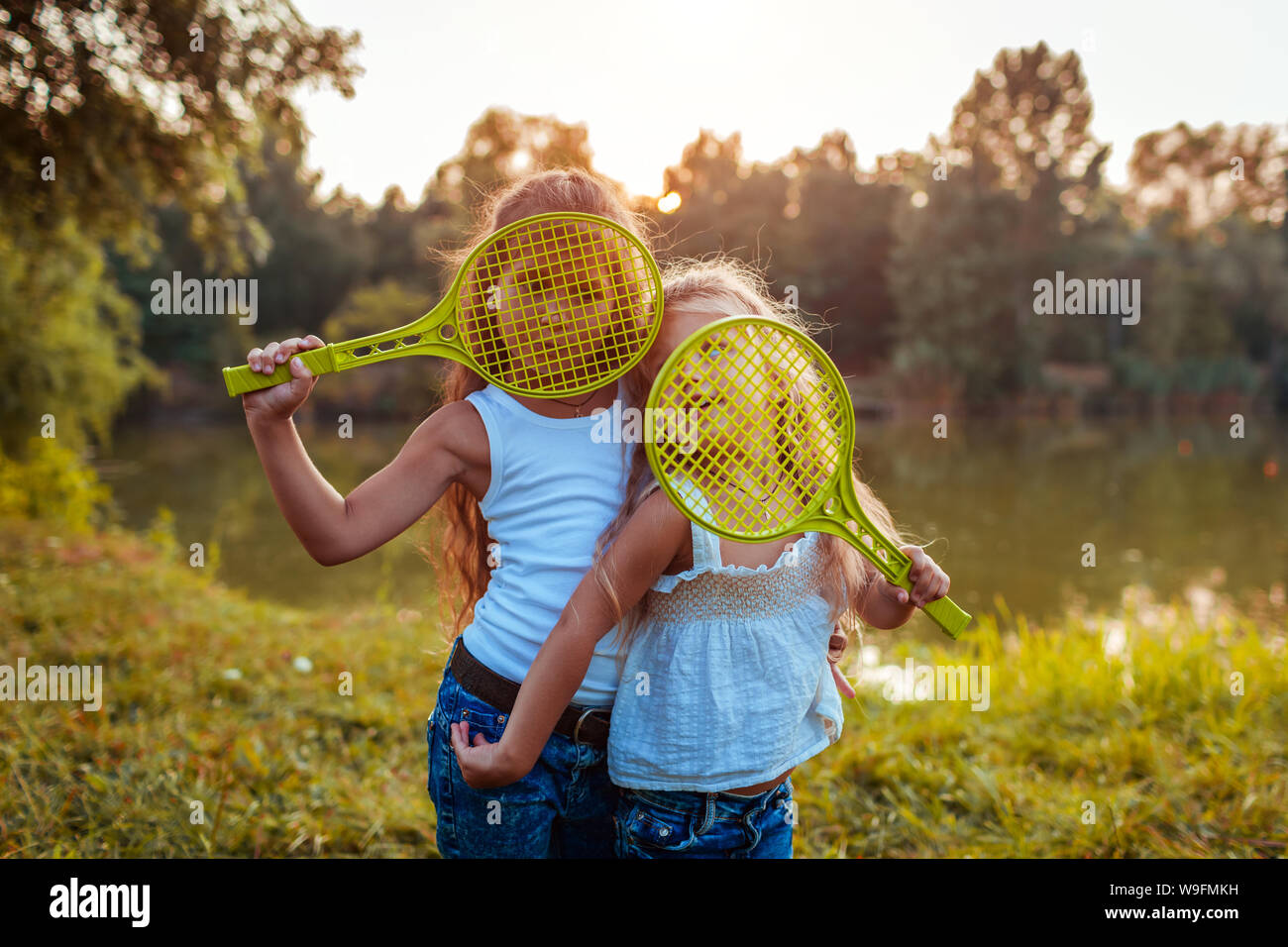Les petites filles s'amuser en plein air après jouer au badminton. Sœurs couvrir visages avec raquettes en été Parc. Les enfants. Journée internationale de Childrens Banque D'Images