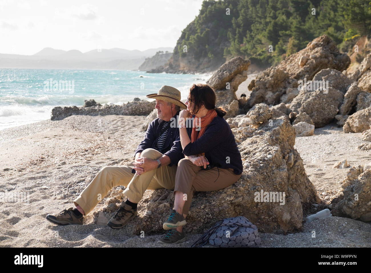 Un couple dans la fin des années 60 début des années 70, s'asseoir et admirer la vue sur la plage isolée et vide Paradissi à Kefalonia, Grèce. Banque D'Images