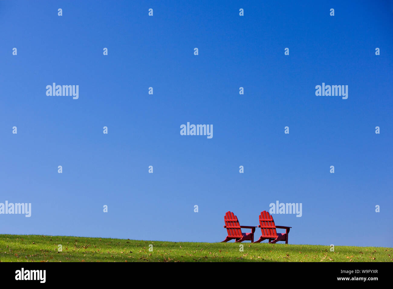 Classique en bois rouge de style Adirondack chaises sont assis sur une colline d'herbe verte. Plan horizontal. Banque D'Images