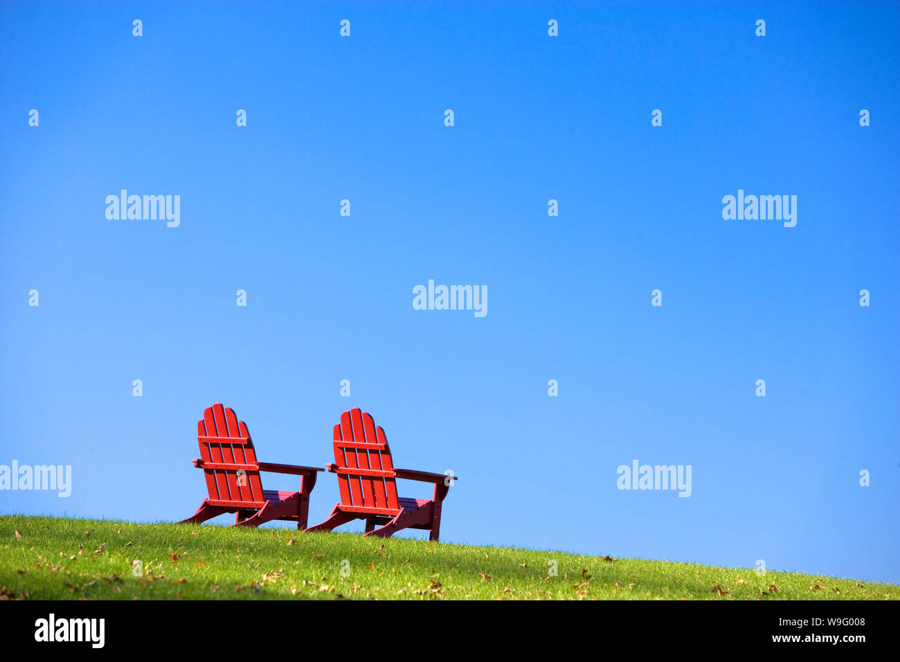 Classique en bois rouge de style Adirondack chaises sont assis sur une colline d'herbe verte. Plan horizontal. Banque D'Images