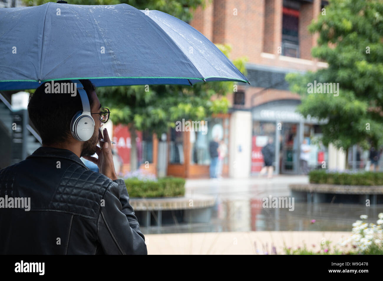 Un homme cherchant un abri contre la pluie fumer une cigarette à un centre commercial Banque D'Images