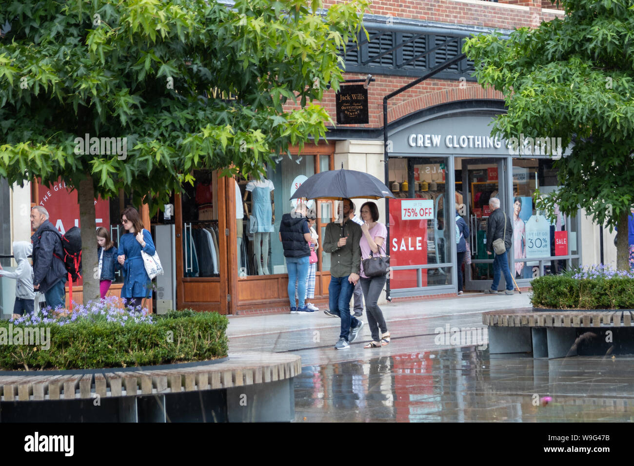 Un couple s'abriter de la pluie sous un parapluie tout en passant devant les vitrines des magasins dans un centre commercial Banque D'Images