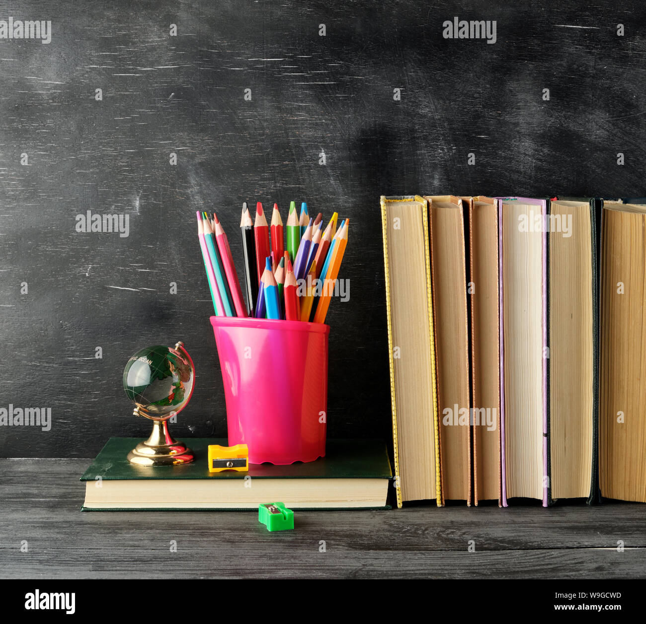 Pile de livres et d'une papeterie bleu verre avec multi-couleur crayons en bois, sur l'arrière-plan d'un tableau noir vide, concept retour à l'école Banque D'Images