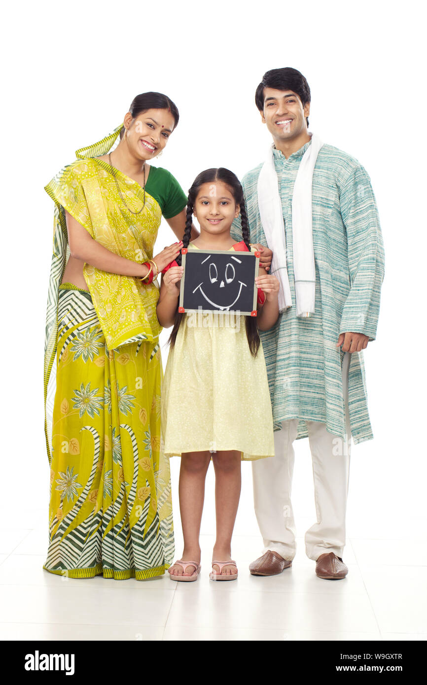 Fille tenant une ardoise visage smiley dessiné sur elle debout avec ses parents Banque D'Images