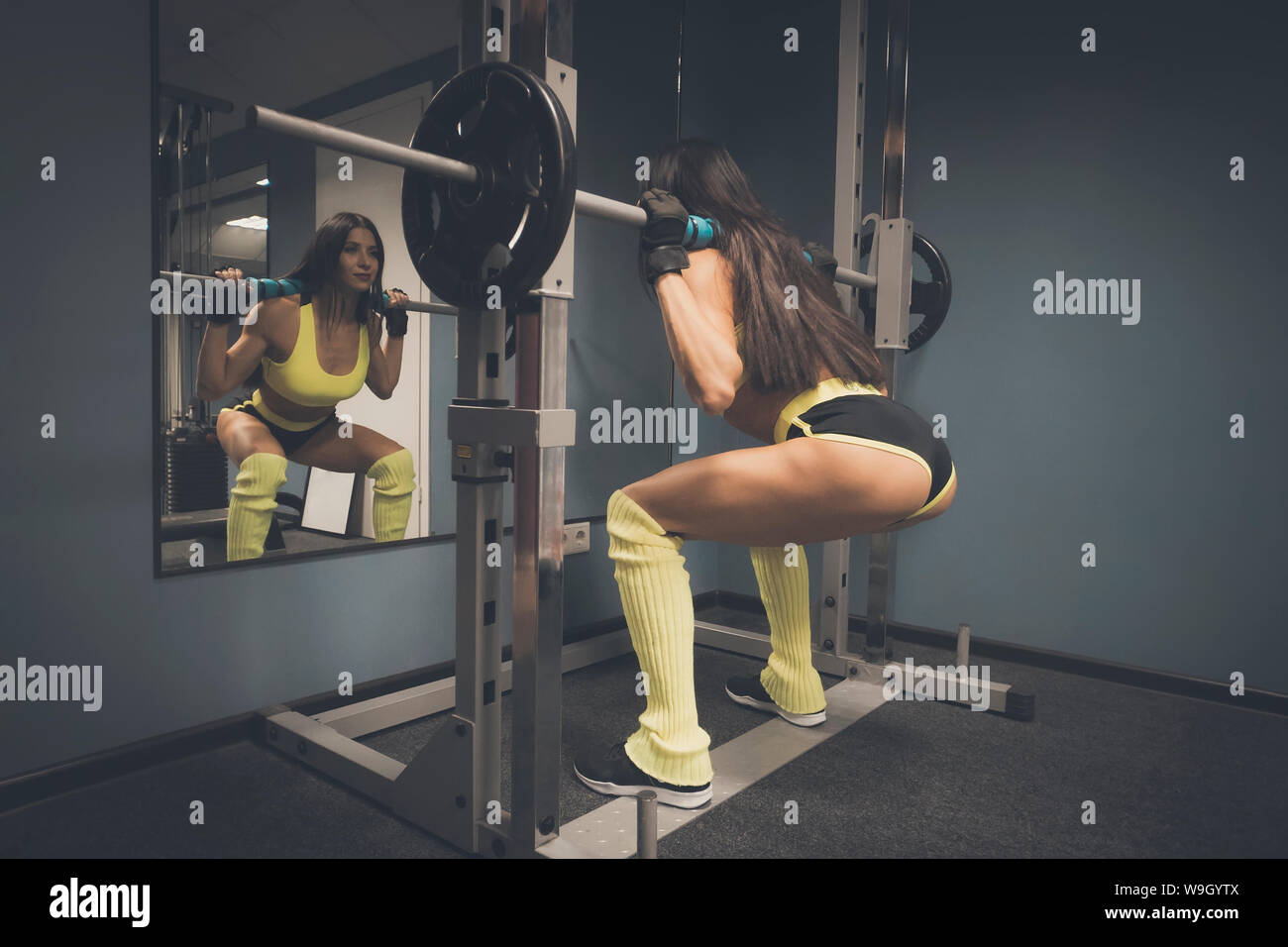La formation de l'athlète féminine dans une salle de sport avant de miroir. Carrossier dans le sport top et short d'entraînement fonctionnel faisant poids de levage. Jolie femme Banque D'Images