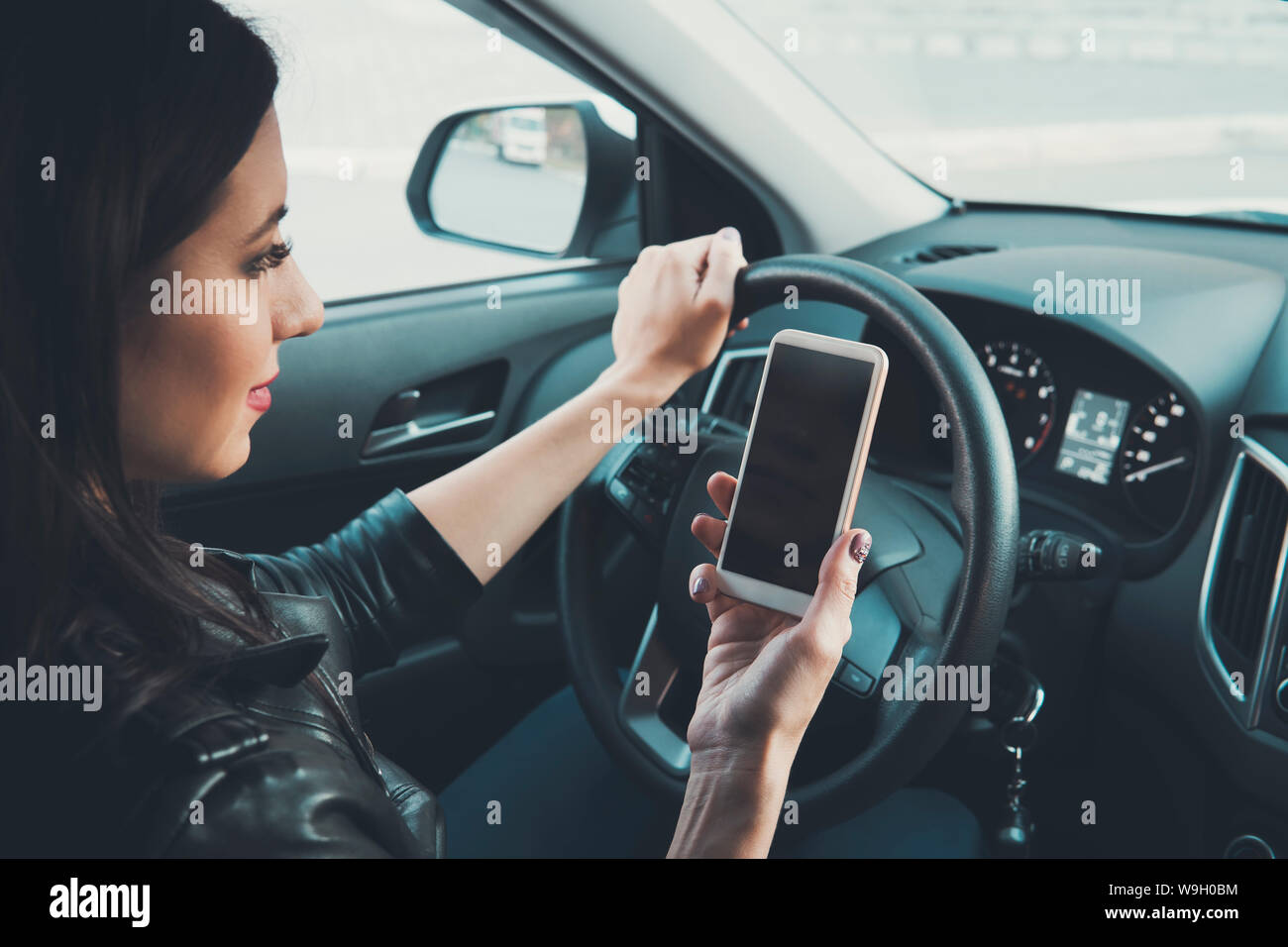 Jeune femme à la recherche de son smartphone au volant d'un véhicule à l'avant arrière-plan de la fenêtre. La pilote distrait. Concept de conduite dangereuse. Femme Banque D'Images